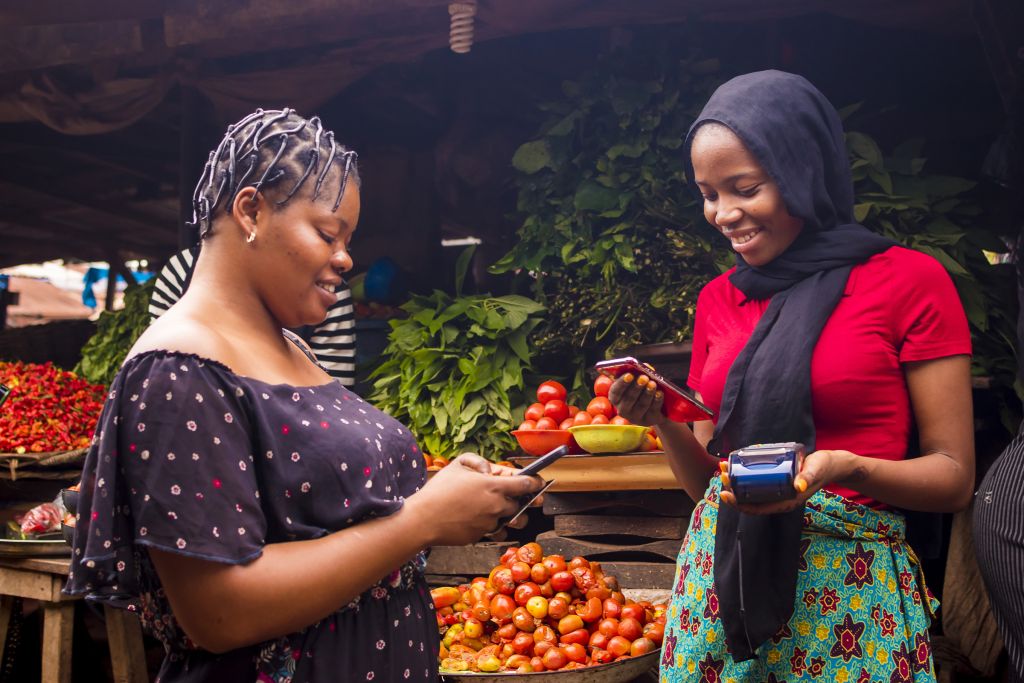 African woman shopping at local market and paying with mobile device.